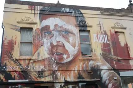 An der Kreuzung der Fitzroy und Johnston Street ist ein bekanntes Porträt eines jungen Aborigines von AWOL.